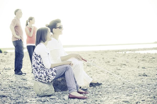 Eine blinde Frau sitzt mit ihrer Familie an einem Ufer .