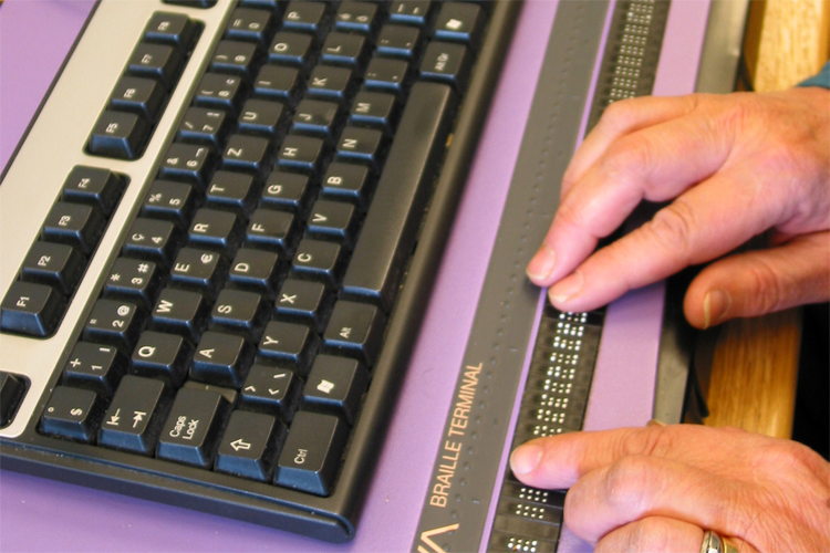Eine blinde Frau tippt auf der Braillezeile an ihrem PC. Bild: SZBLIND