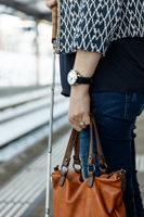 Eine Frau steht am Bahngleis mit ihrem Blindenstock und wartet auf den Zug. Sie hat eine Handtasche bei sich und trägt die ACUSTICA am Handgelenk.